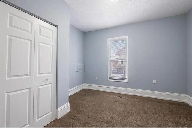 2723 Dupont Ave N, Minneapolis, MN 55411 - unfurnished bedroom with dark colored carpet, a textured ceiling, baseboards, and a closet