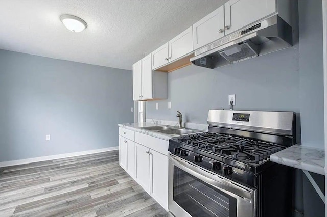 2723 Dupont Ave N, Minneapolis, MN 55411 - kitchen with gas stove, under cabinet range hood, a sink, light wood finished floors, and white cabinets
