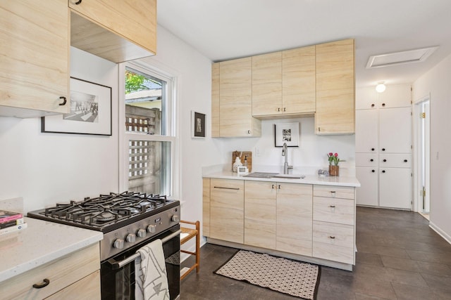 kitchen featuring stainless steel range with gas stovetop, light brown cabinetry, a sink, and light stone countertops
