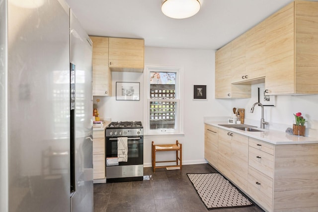 kitchen with appliances with stainless steel finishes, light brown cabinetry, a sink, light countertops, and baseboards