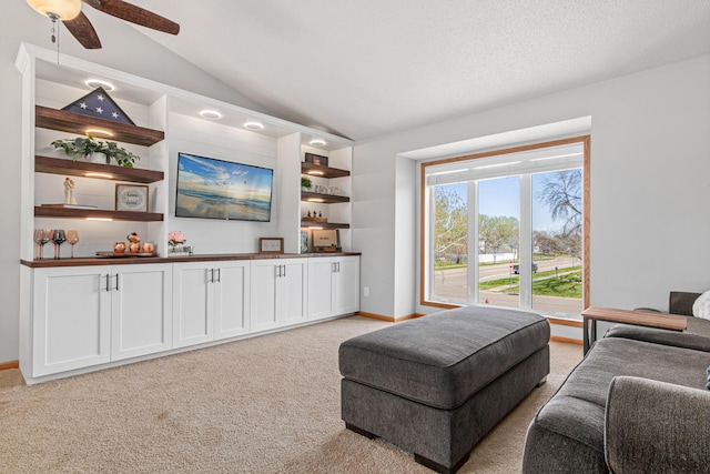 living room featuring light colored carpet, lofted ceiling, baseboards, and a ceiling fan