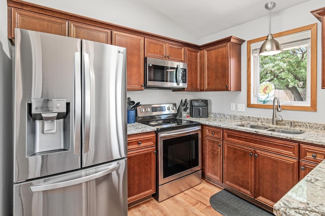 kitchen featuring appliances with stainless steel finishes, a sink, lofted ceiling, light wood finished floors, and brown cabinetry