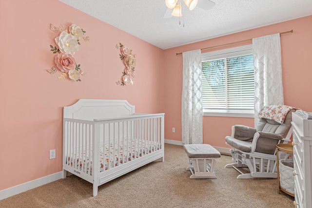 bedroom with carpet flooring, a crib, a textured ceiling, and baseboards