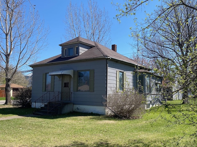 bungalow featuring a front lawn, a chimney, and roof with shingles
