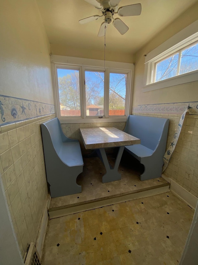 dining area featuring tile walls, a wainscoted wall, and a ceiling fan
