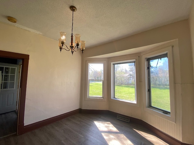 unfurnished dining area with wood finished floors, a textured ceiling, a chandelier, and baseboards