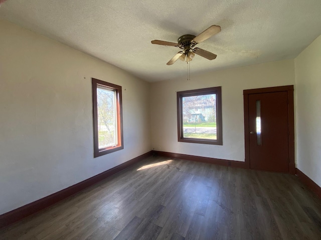 spare room with plenty of natural light, dark wood finished floors, a textured ceiling, baseboards, and a ceiling fan