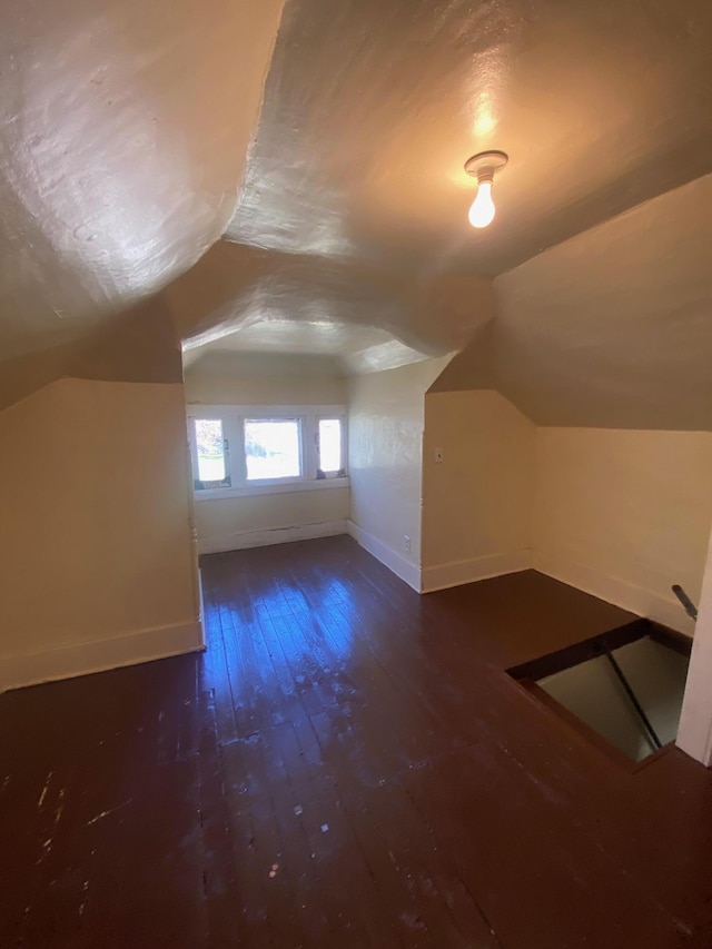 additional living space with baseboards, wood-type flooring, and vaulted ceiling