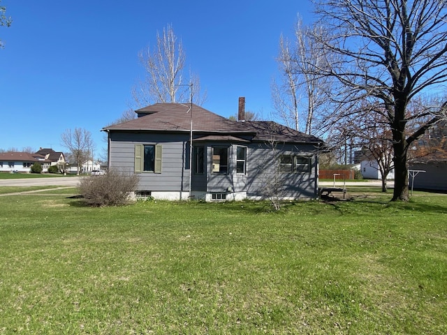 rear view of property with a lawn, a chimney, and roof with shingles