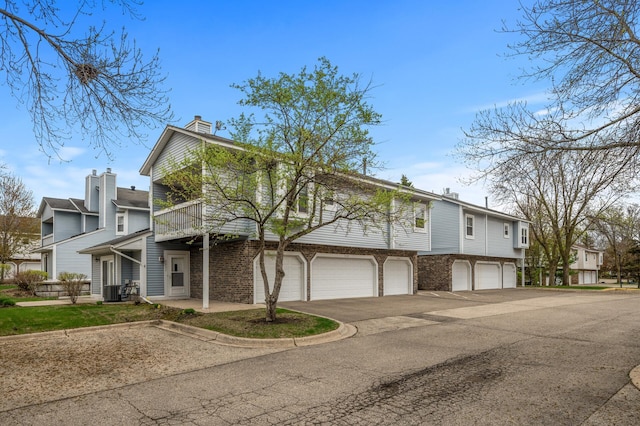 view of front of home with a garage, a balcony, asphalt driveway, a chimney, and a residential view