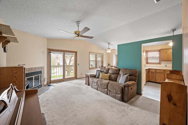 living area featuring light colored carpet, ceiling fan, lofted ceiling, a fireplace, and a textured ceiling