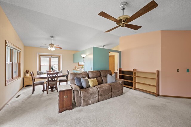 living area with ceiling fan, light carpet, vaulted ceiling, and baseboards