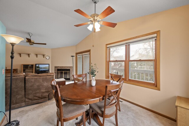 dining room featuring a ceiling fan, light colored carpet, a fireplace, vaulted ceiling, and baseboards
