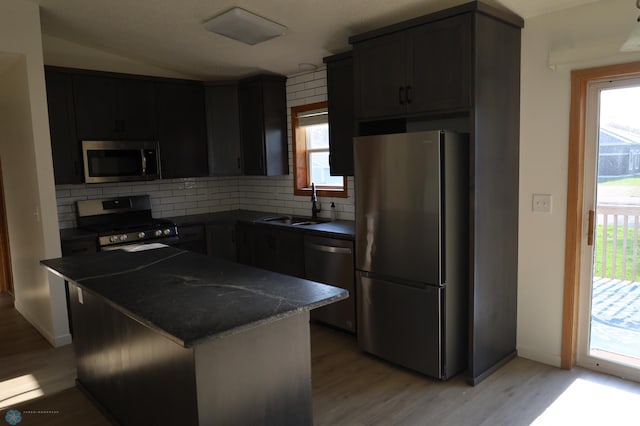 kitchen with stainless steel appliances, dark countertops, a sink, tasteful backsplash, and light wood-type flooring