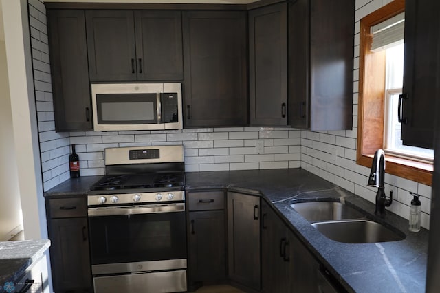 kitchen featuring stainless steel appliances, a sink, backsplash, and dark stone counters