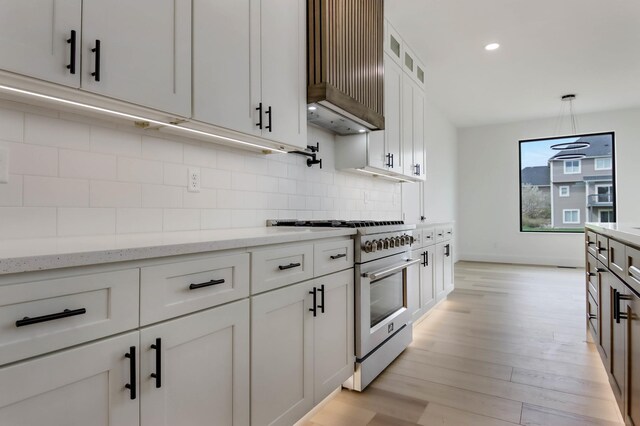 1796 Cobblestone Ct, Hastings, MN 55033 - kitchen featuring stainless steel range, wall chimney exhaust hood, white cabinets, backsplash, and light wood-style floors