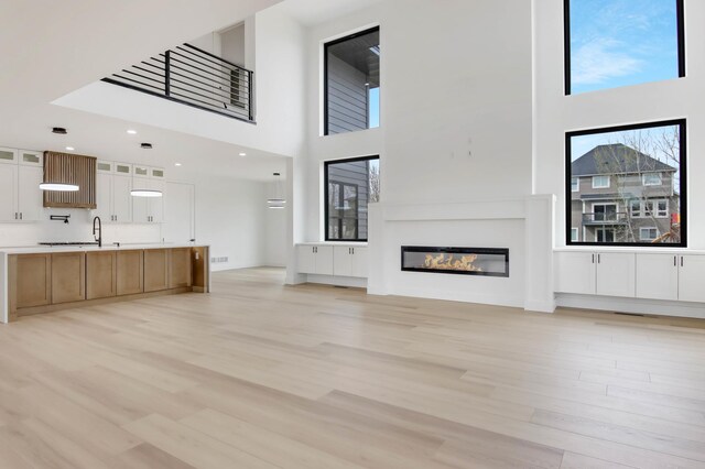 1796 Cobblestone Ct, Hastings, MN 55033 - unfurnished living room with light wood-style flooring, a towering ceiling, a glass covered fireplace, and a sink