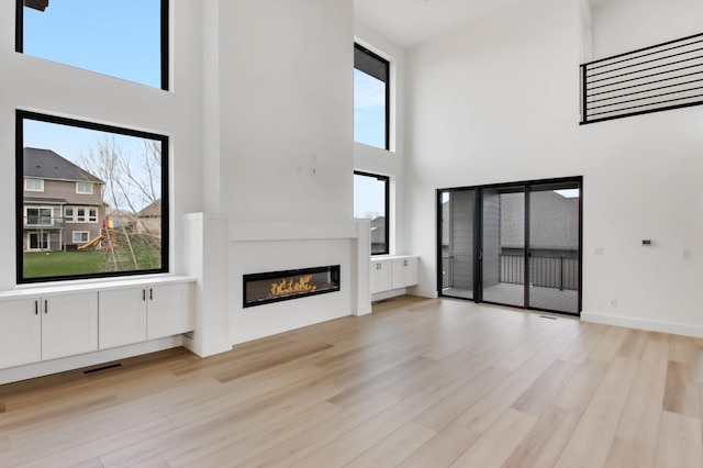 1796 Cobblestone Ct, Hastings, MN 55033 - unfurnished living room featuring a towering ceiling, light wood-type flooring, and a glass covered fireplace