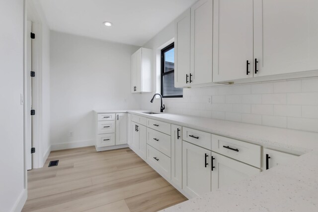1796 Cobblestone Ct, Hastings, MN 55033 - kitchen featuring a sink, tasteful backsplash, light wood-style flooring, white cabinetry, and baseboards