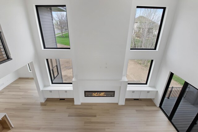 1796 Cobblestone Ct, Hastings, MN 55033 - unfurnished living room featuring light wood-style floors, a glass covered fireplace, baseboards, and a towering ceiling