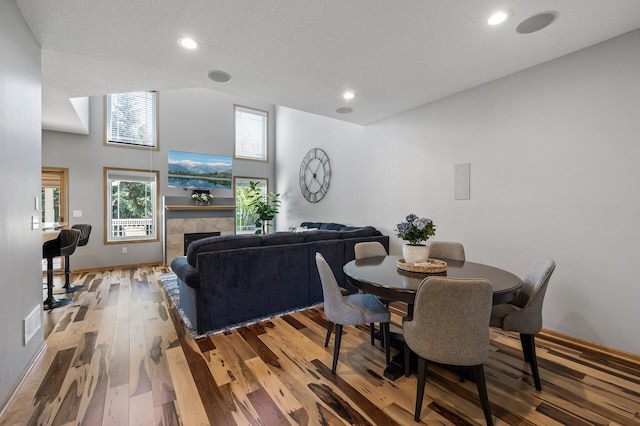 dining area featuring wood finished floors, a textured ceiling, a tile fireplace, baseboards, and recessed lighting