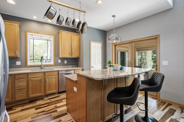 kitchen featuring stainless steel appliances, a sink, light wood-style floors, a center island, and a kitchen breakfast bar