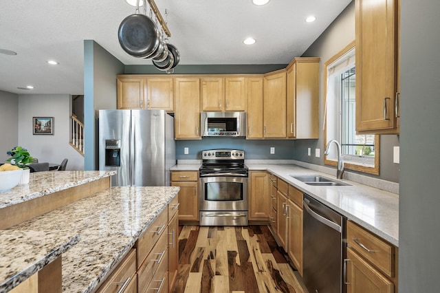kitchen with appliances with stainless steel finishes, a sink, light wood-type flooring, recessed lighting, and light stone counters