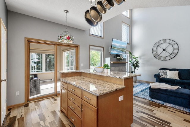 kitchen featuring light wood-style floors, open floor plan, a center island, light stone counters, and pendant lighting
