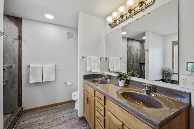 bathroom with wood finished floors, a shower stall, toilet, double vanity, and baseboards