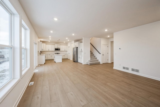 unfurnished living room with light wood-type flooring, baseboards, stairs, recessed lighting, and a sink