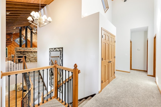 hallway with a high ceiling, an upstairs landing, a chandelier, carpet, and baseboards