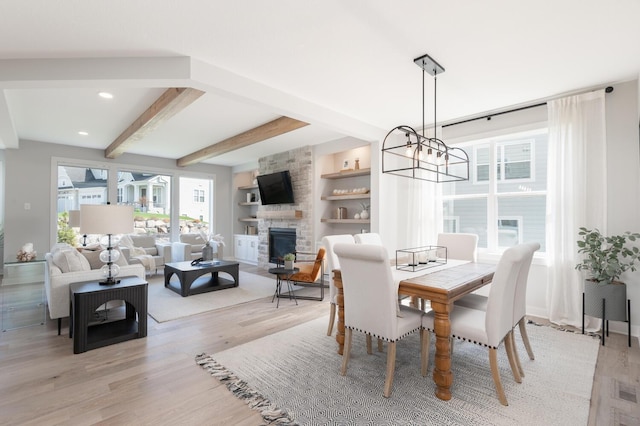 dining area with light wood finished floors, beamed ceiling, a chandelier, a stone fireplace, and recessed lighting