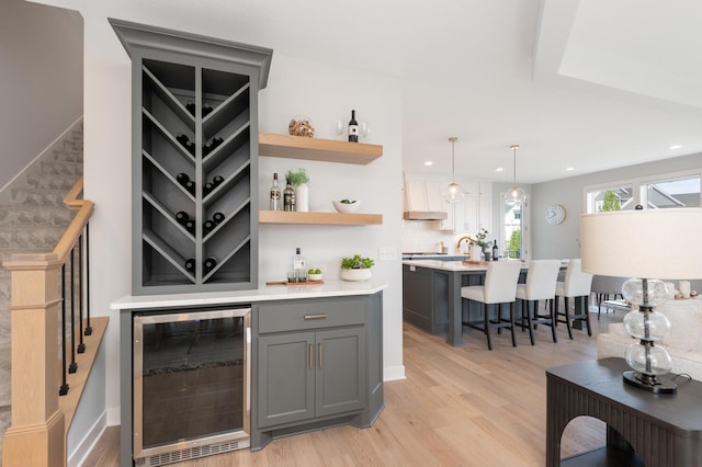 indoor dry bar featuring wine cooler, light wood finished floors, recessed lighting, tasteful backsplash, and stairway