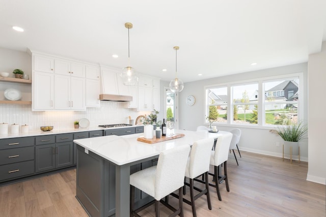 kitchen with gray cabinetry, stainless steel gas cooktop, open shelves, tasteful backsplash, and light countertops