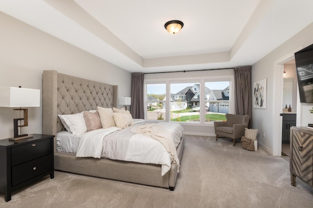 bedroom featuring a raised ceiling, light carpet, and baseboards