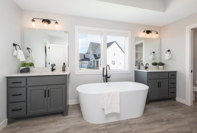 bathroom with a soaking tub, wood finished floors, two vanities, and toilet