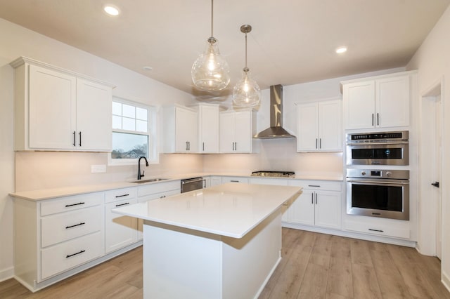 kitchen featuring wall chimney range hood, a sink, stainless steel appliances, light wood-type flooring, and white cabinets