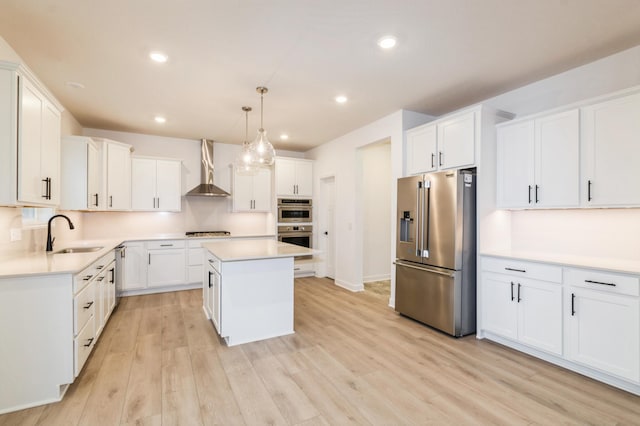 kitchen with appliances with stainless steel finishes, wall chimney exhaust hood, a sink, light countertops, and recessed lighting