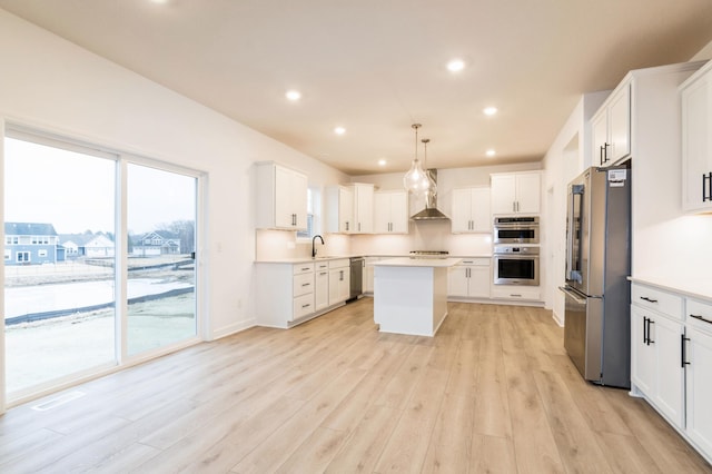 kitchen with appliances with stainless steel finishes, a sink, a kitchen island, light wood-style flooring, and light countertops