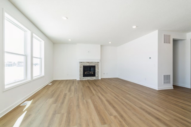 unfurnished living room with light wood-type flooring, baseboards, recessed lighting, and a stone fireplace