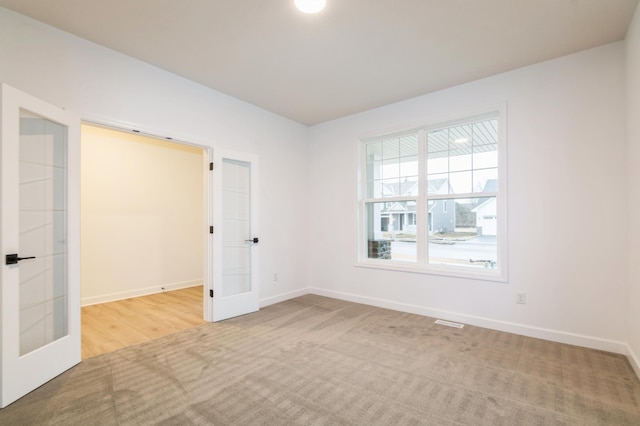 carpeted empty room featuring french doors and baseboards