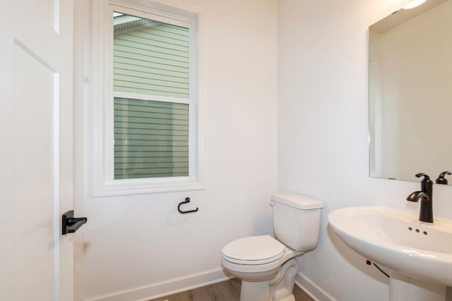 half bath featuring a sink, baseboards, wood finished floors, and toilet