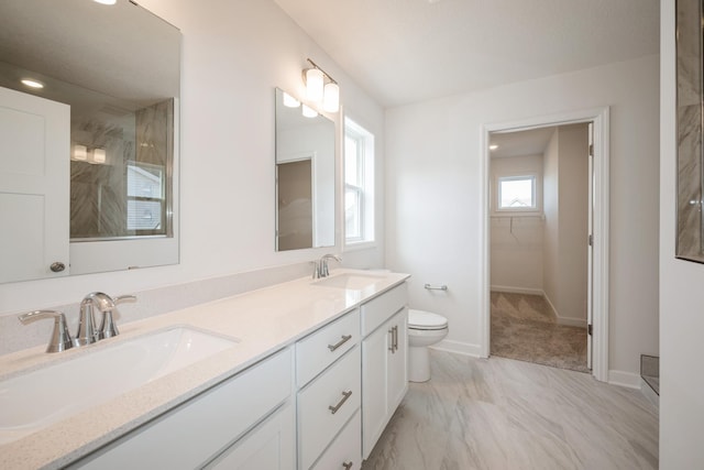bathroom featuring toilet, marble finish floors, double vanity, baseboards, and a spacious closet