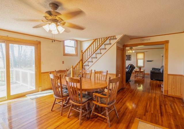 dining area with a ceiling fan, a wainscoted wall, wood finished floors, a textured ceiling, and wooden walls