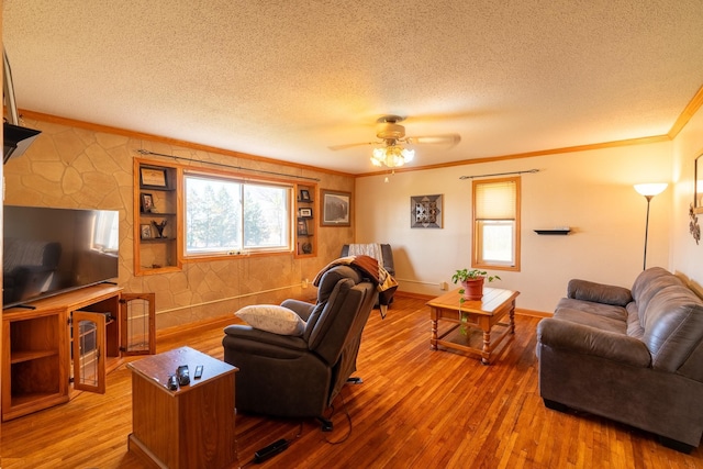 living area with a textured ceiling, ornamental molding, wood finished floors, a ceiling fan, and baseboards