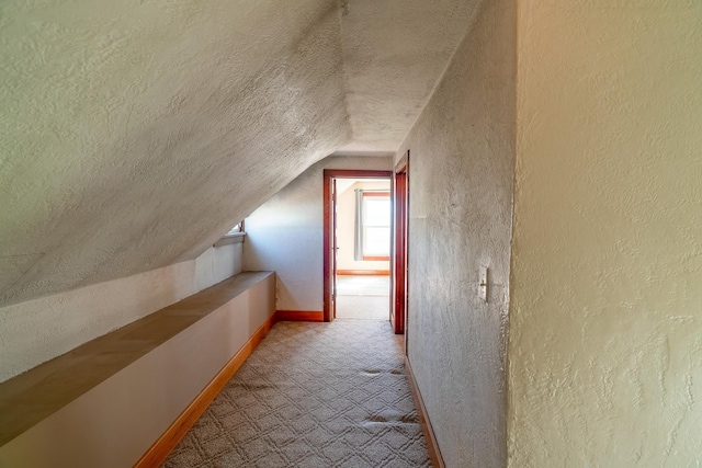 additional living space featuring a textured wall, lofted ceiling, a textured ceiling, and baseboards