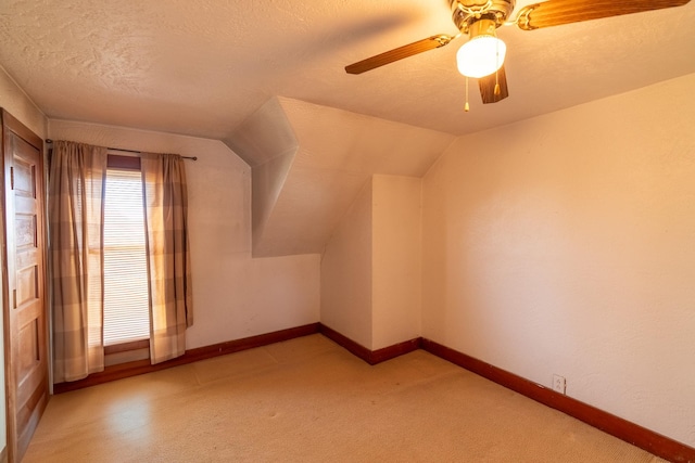 additional living space featuring a textured ceiling, a ceiling fan, light colored carpet, baseboards, and lofted ceiling