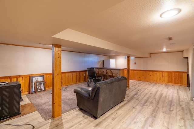 living area featuring a wainscoted wall, wooden walls, light wood-type flooring, a dry bar, and a textured ceiling