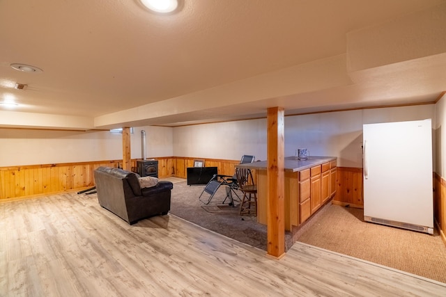 finished basement with freestanding refrigerator, wainscoting, light wood finished floors, and wooden walls