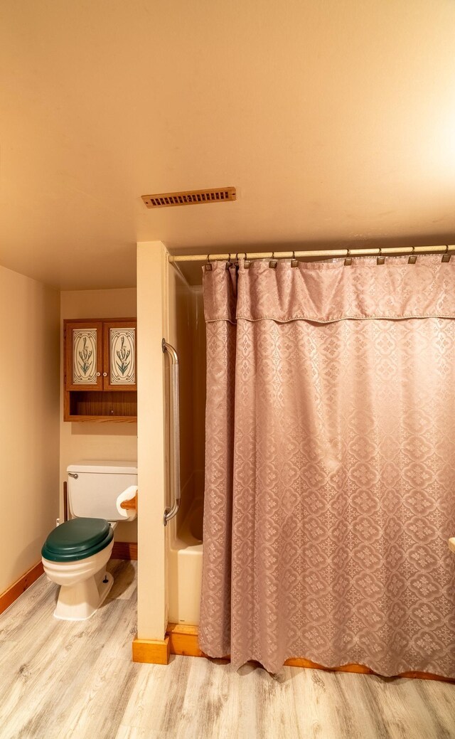 full bathroom featuring wood finished floors, toilet, shower / bath combo with shower curtain, and baseboards